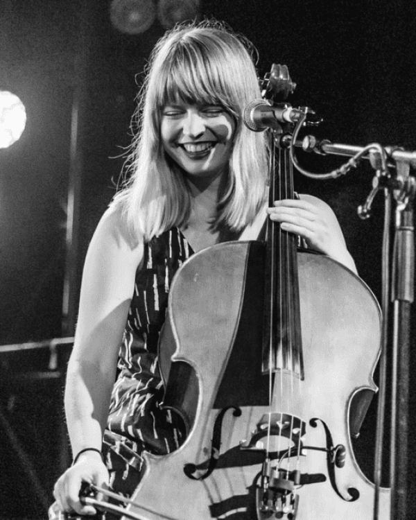 Cellist & singer songwriter Monique Clare on stage with her cello, smiling.